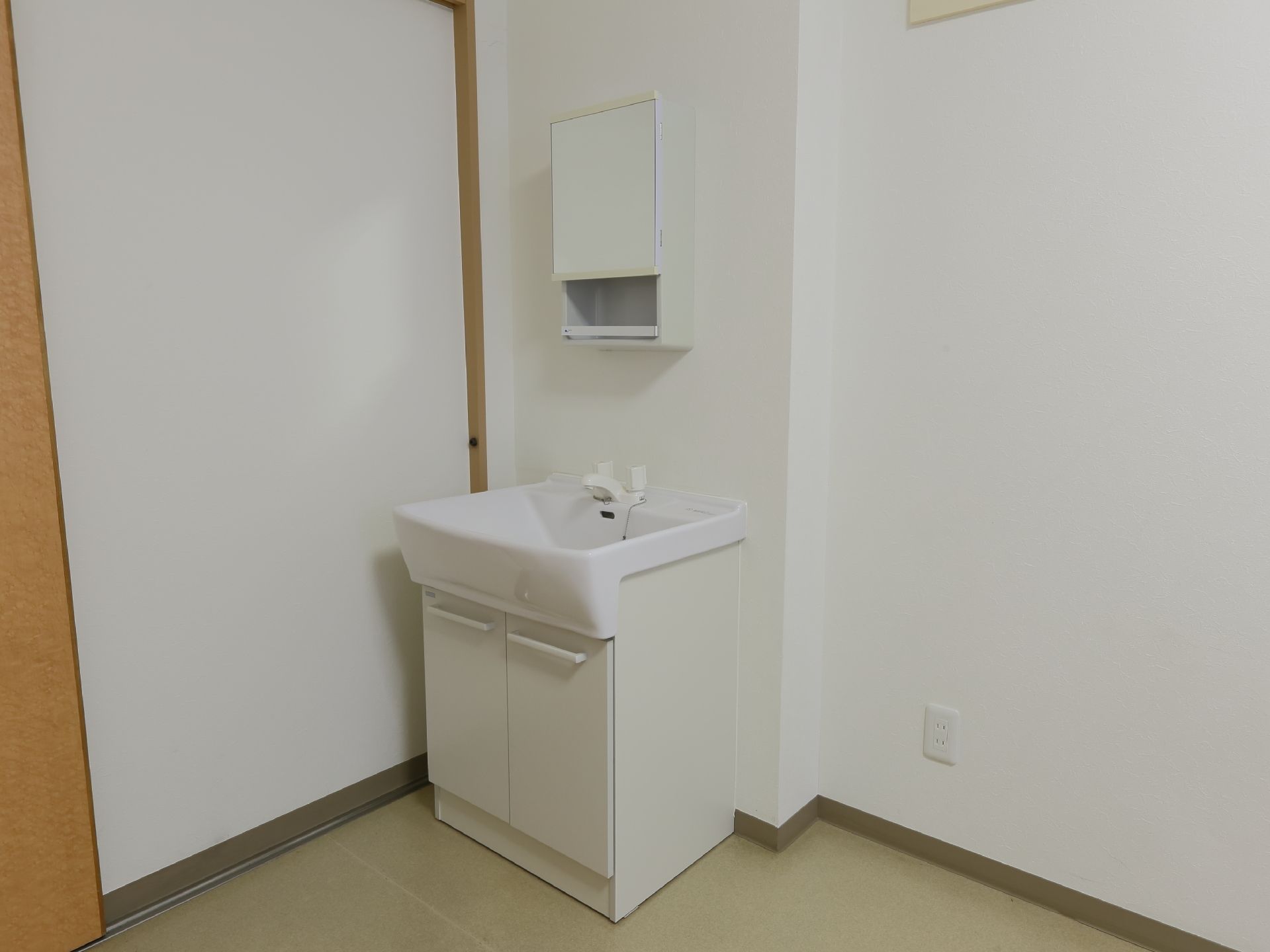 居室に備えられた白色で統一された洗面台である。下には両開きの収納庫があり、上部には鏡付きの棚ボックスが備えられている。