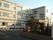 白とベージュが基調の３階建ての建物に、グレーの横ラインが引いてあるデザインになっている。建物の前には駐車場や花壇が作られている。