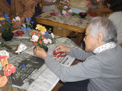 テーブルの周りに集まって、色とりどりの花で生け花を楽しんでいる入居者様たち