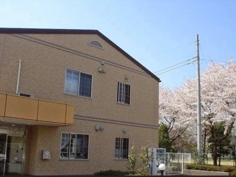 外壁がブラウンの２階建て施設である。ひさし付きのエントランスが設けられている。壁際には、自販機が設置されている。
