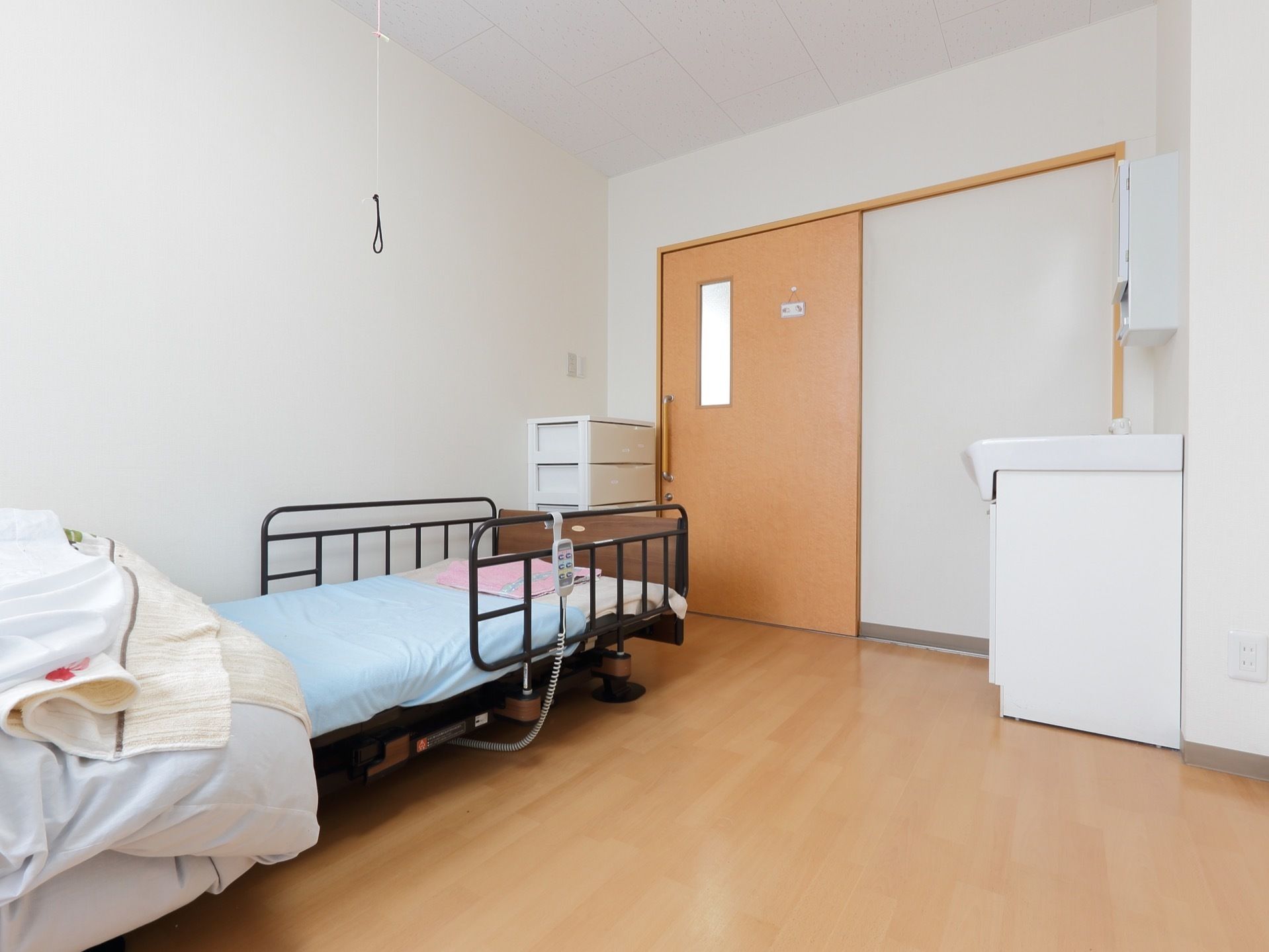 居室の扉は大きな引き戸であり、出入りをスムーズに行える。電動ベッドで自分で高さ調整ができるため、ベッドへの立ち上がりなど容易にできる。