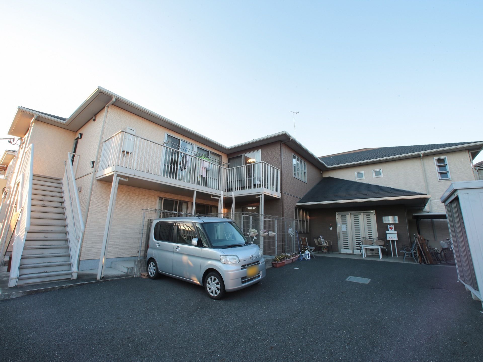 ベランダ付きの２階建ての施設には、非常階段が設置されている。建物前に駐車場や駐輪場が設けられている。