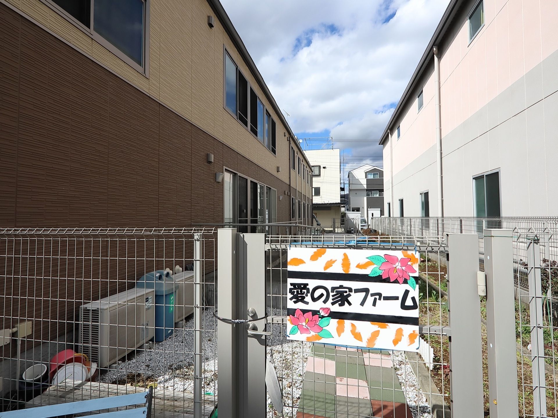 勝手口に、白地の板にカラフルな色づかいの花や葉っぱが描かれた看板が設置されている。扉はチェーンロックされている。