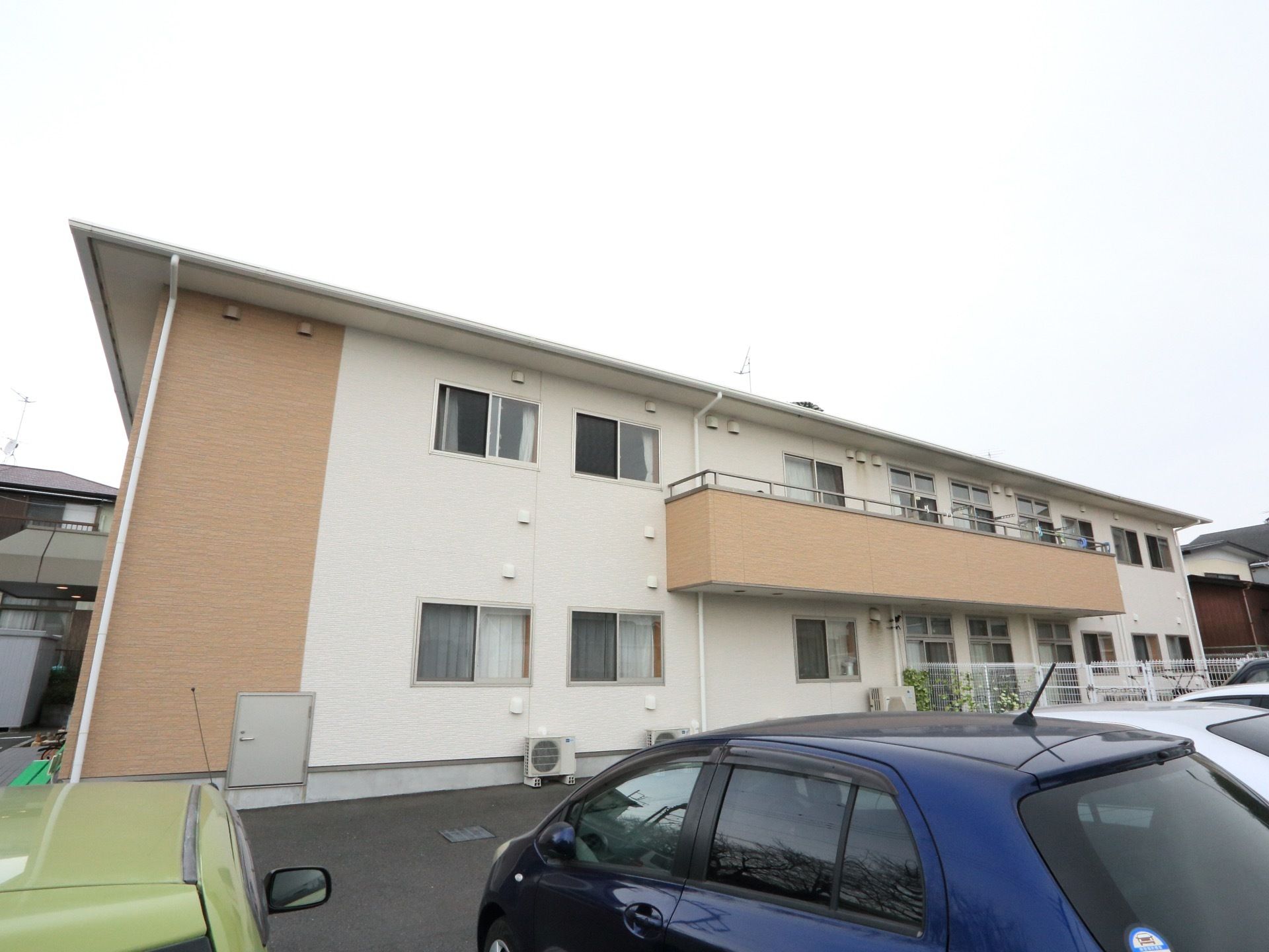 施設の外観の様子。アパートのような造りで、2階建ての建物である。バルコニーがあり、施設の手前には駐車場がある。