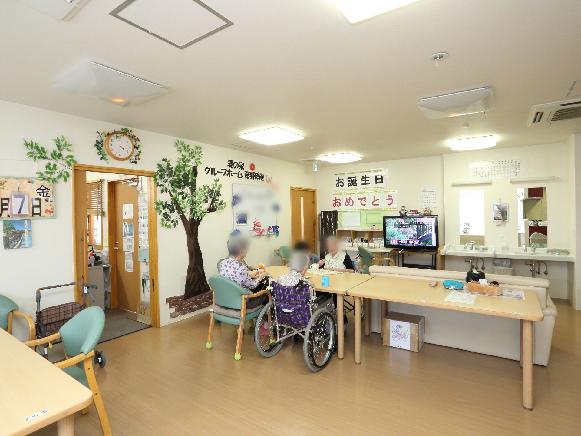通常の椅子と車椅子が並んで座ることのできる幅に余裕のあるダイニングテーブル。壁には木の絵が張り付けられている。
