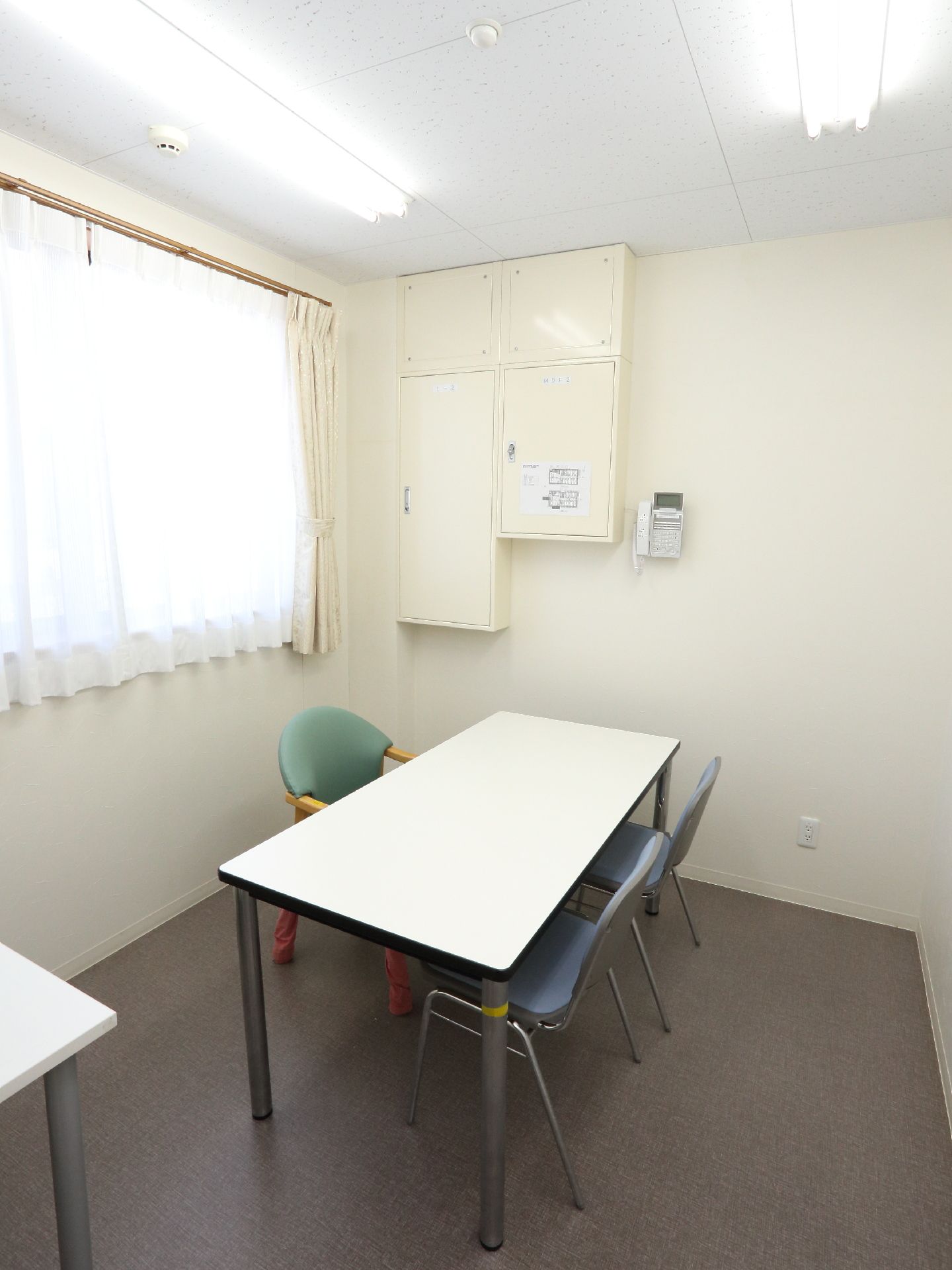 面談のできる椅子とテーブルがある。壁面に電話が設置されている。窓が大きく日当たりが良い。コンセントもつなげる。