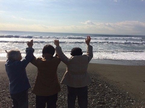 日が差す大海原に向かって両手を挙げている３名の背中からの写真