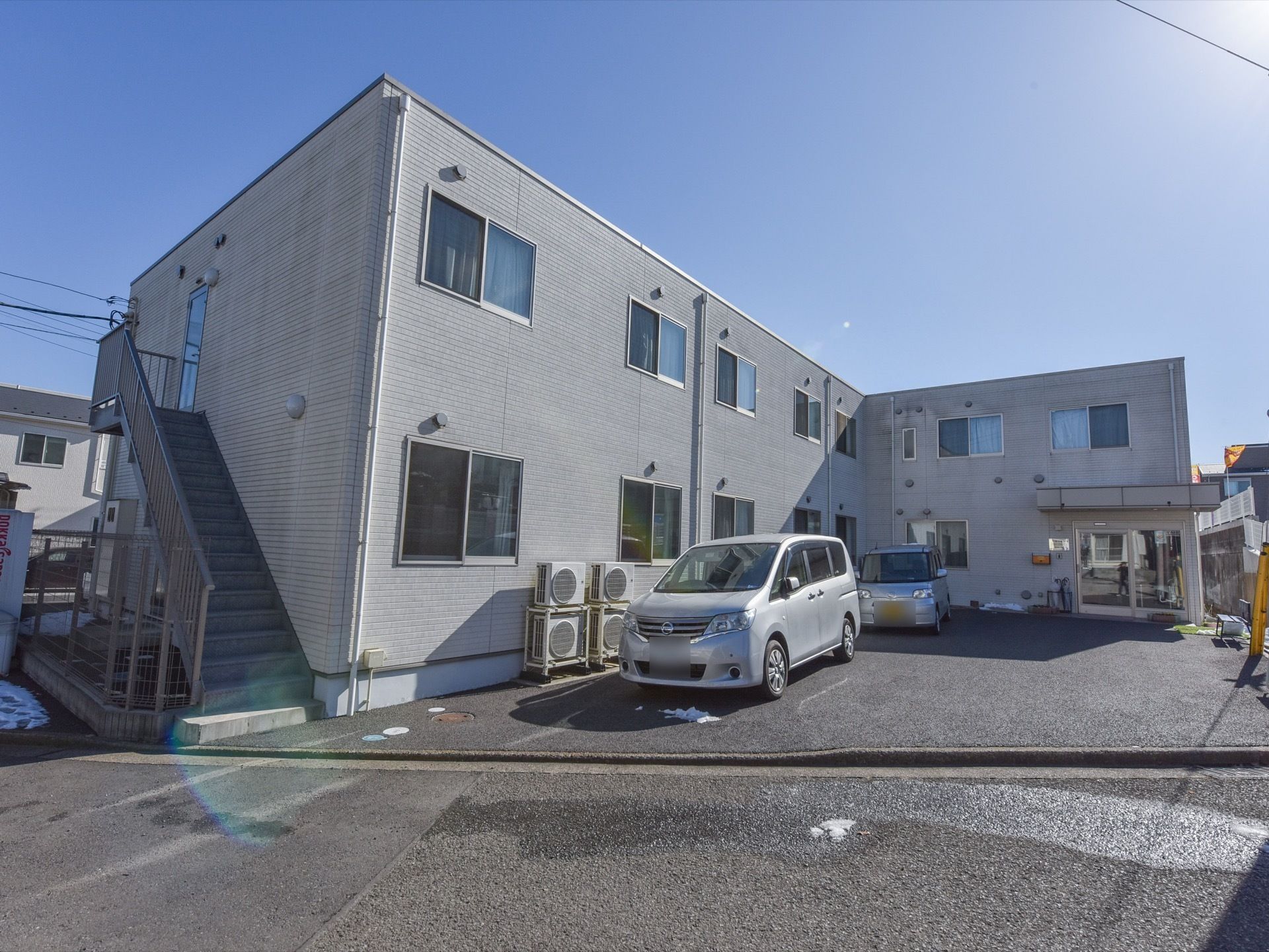 施設の建物は２階建てで、屋根は平らである。向かって左側に外階段が完備されており、施設はフェンスに囲まれている。
