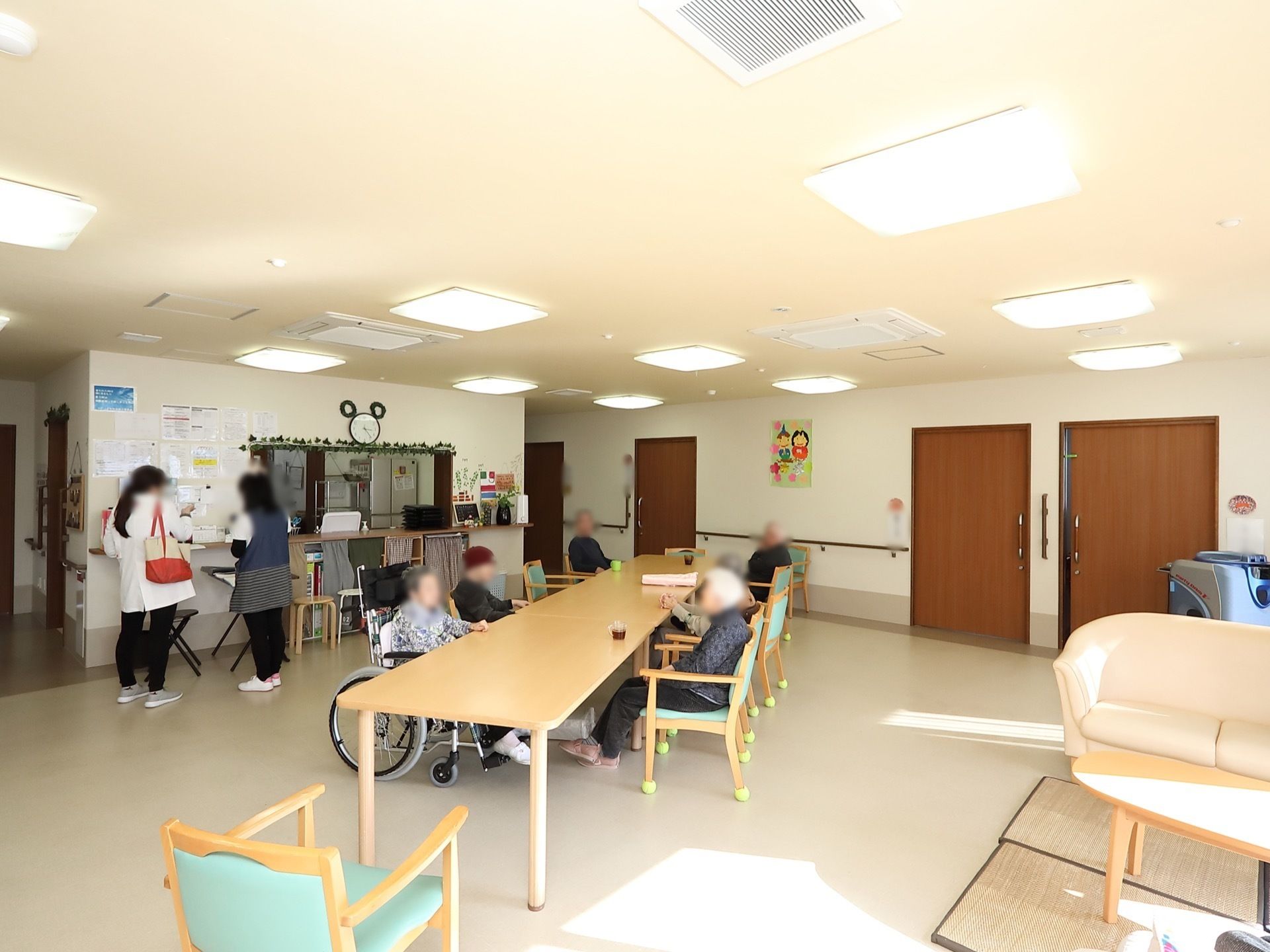 白っぽい床色の共有スペースである。広々としたテーブルが置かれており、入居者様が憩いの時間を過ごしている。