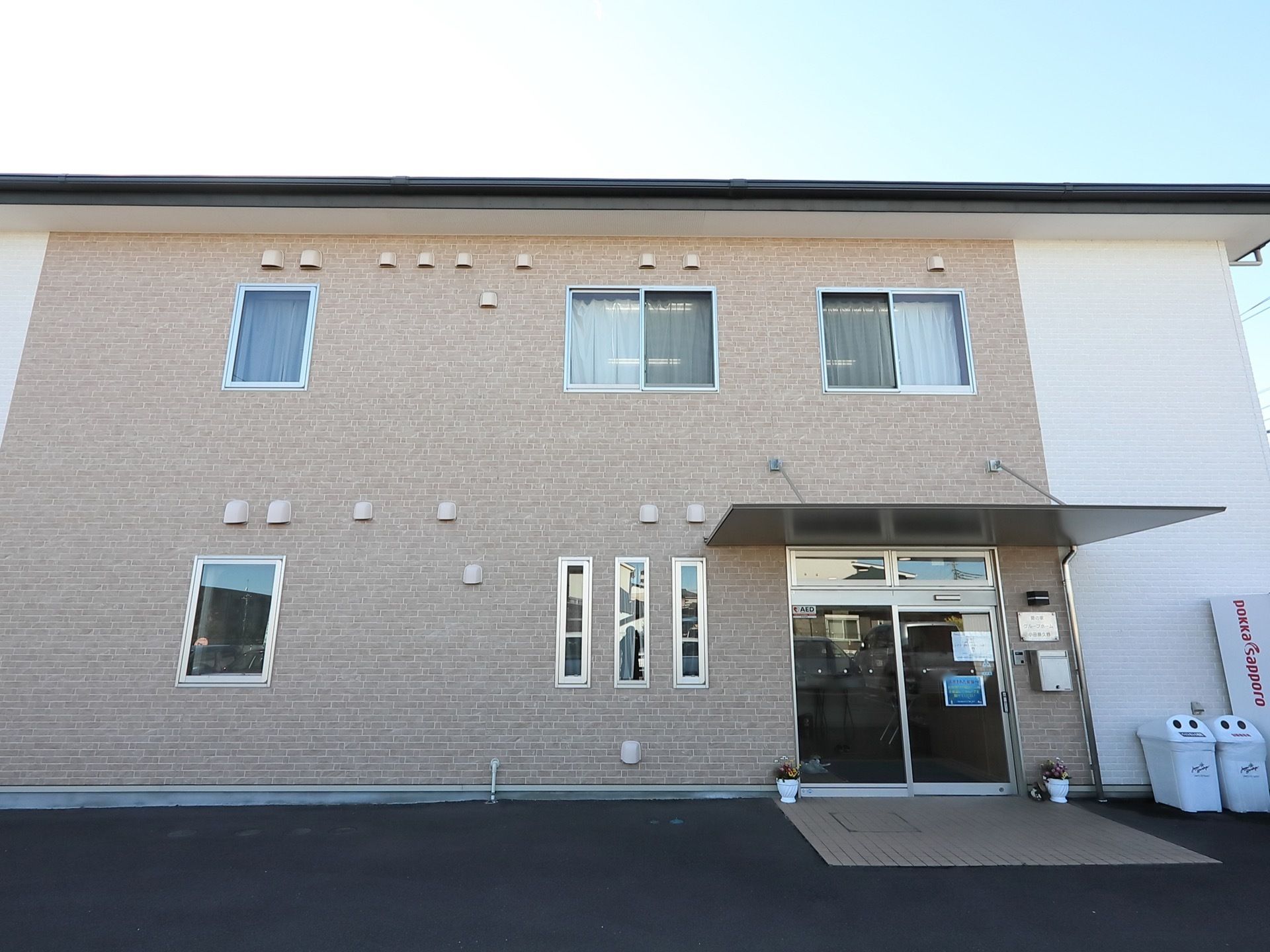 白色とベージュ色を基調とした２階建ての施設である。玄関の上には、大きなひさしが設置されている。玄関横には自動販売機がある。