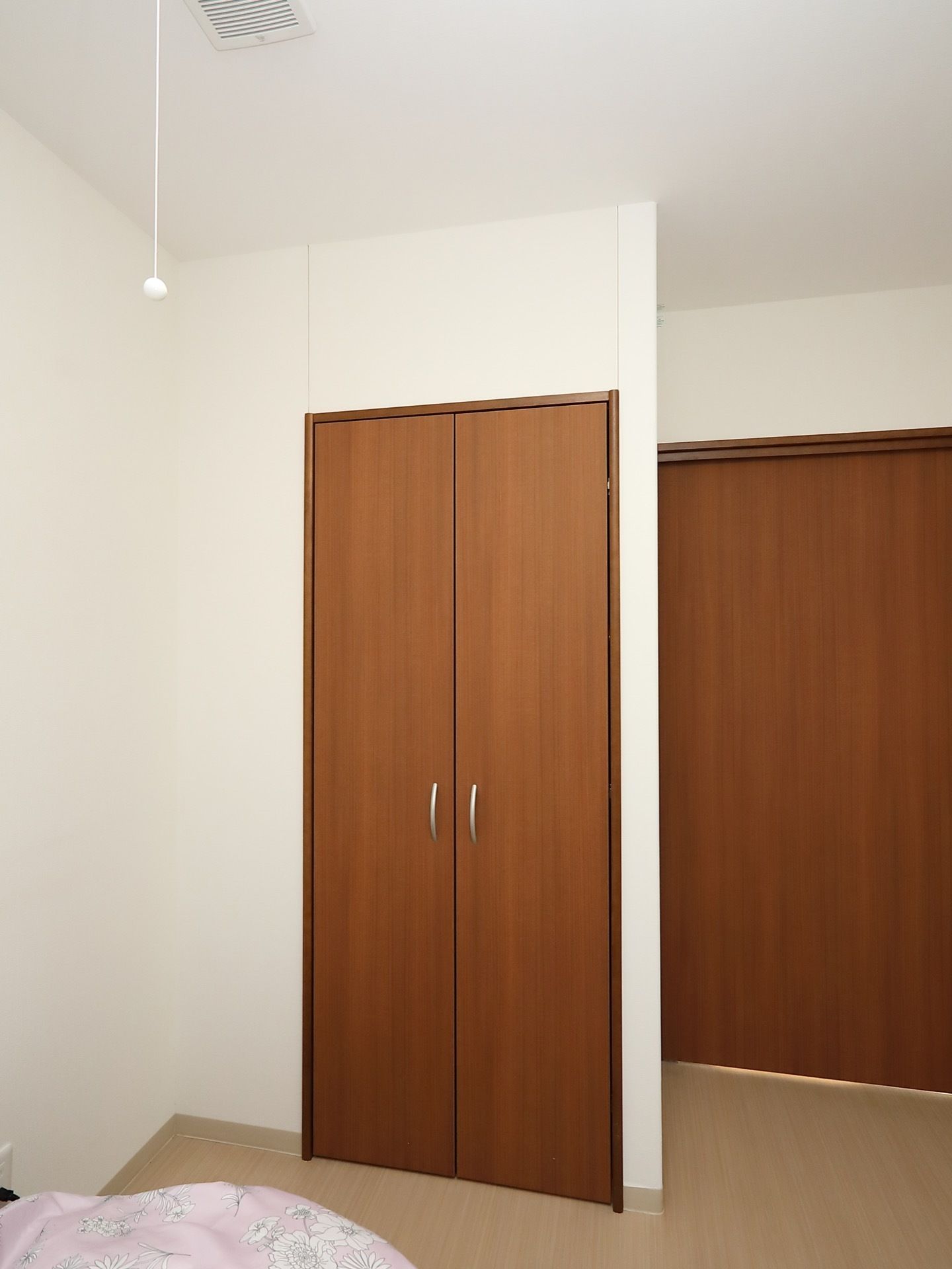 居室入口の扉は、茶色の大きな引き戸になっている。室内には、背の高い観音開きの扉の収納スペースがある。