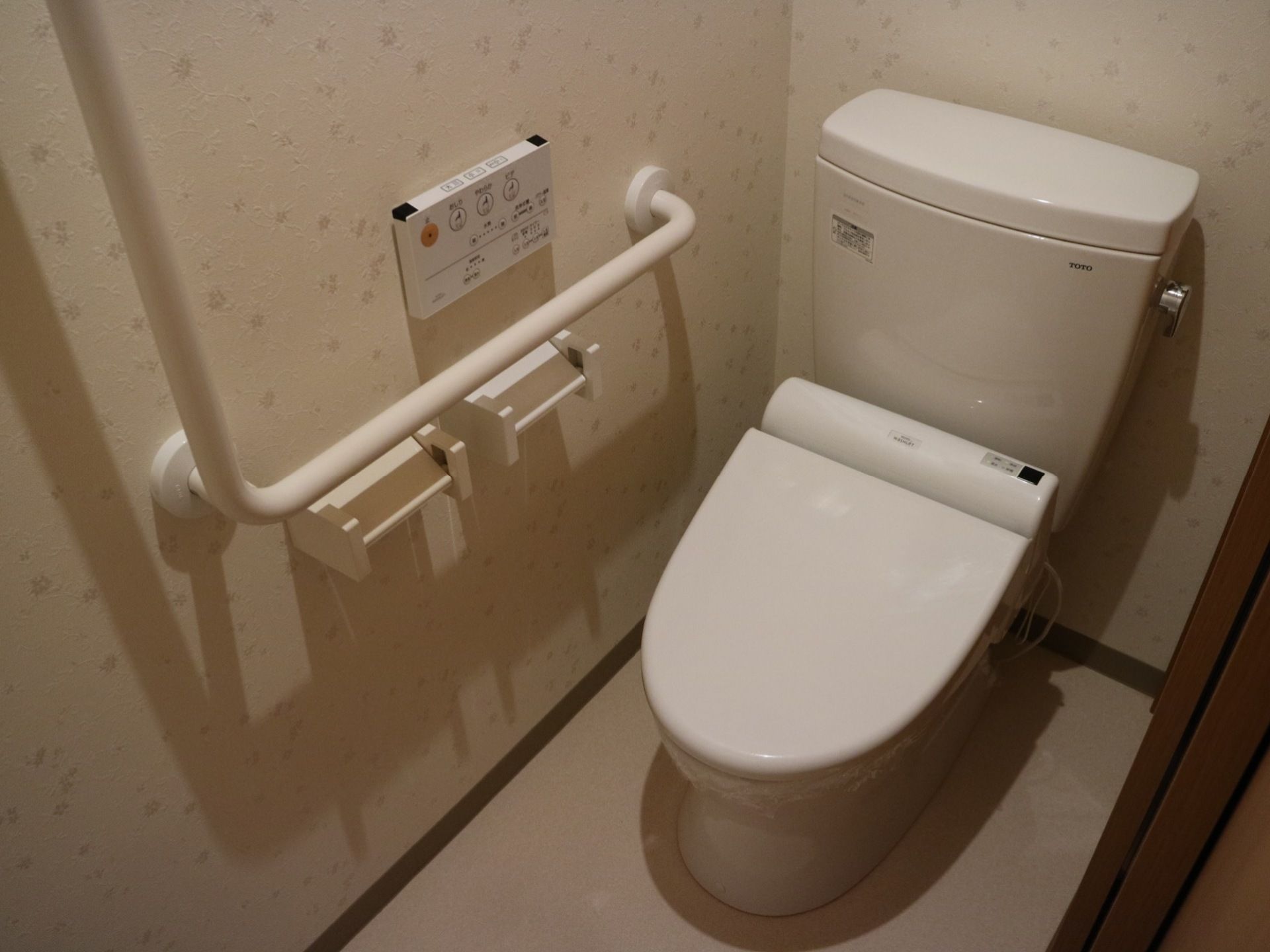 居室に付属しているトイレである。全体的に白色で構成されており、清潔感がある。温水洗浄便座仕様で、壁には長い手すりが設置されている。