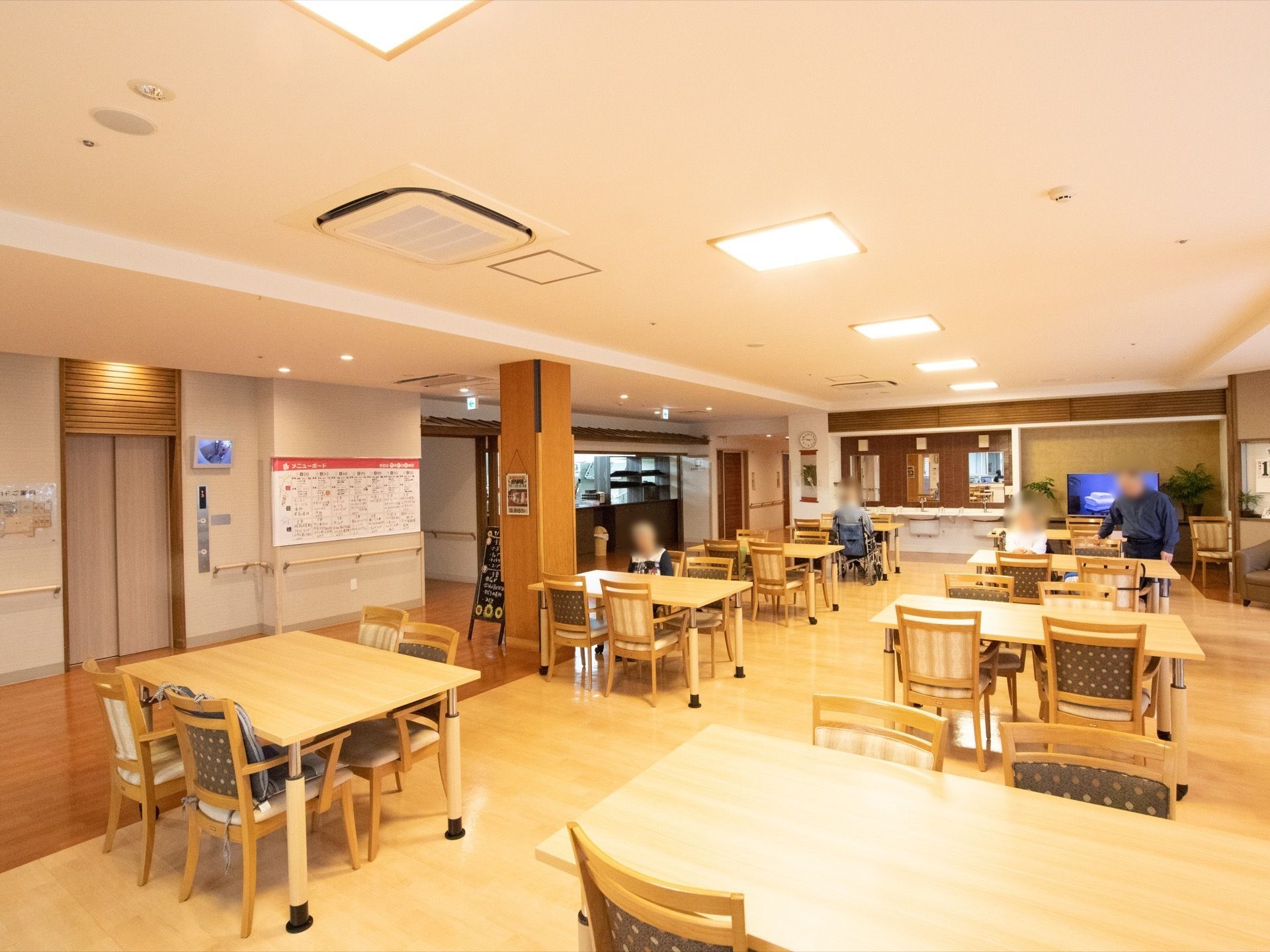 広々とした食堂で入居者様が食事を召し上がっている。洗面所がついているので手洗い、うがいが徹底できる。