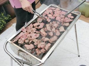 トングを使って、バーベキューコンロで肉を焼く様子