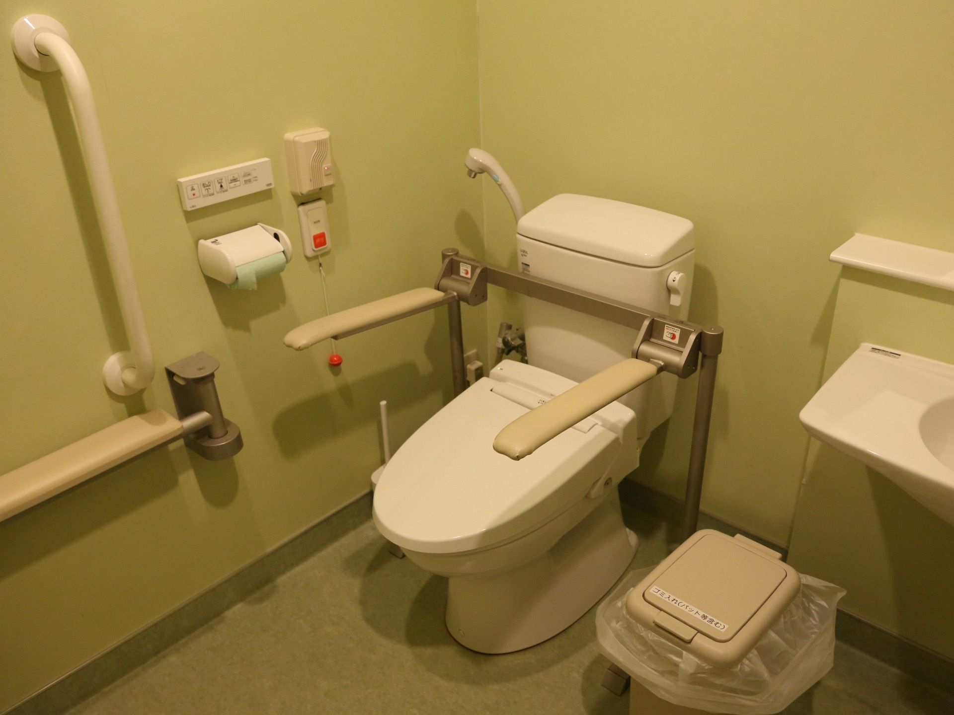 トイレの壁と床はグリーンで統一され、落ち着いた雰囲気になっている。便器の脇には可動式の手すりと緊急通報装置が設置されている。