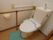 室内には、タンク付きのトイレが1つ設置されている。便座前の床には、水色の小さなマットが敷かれている。