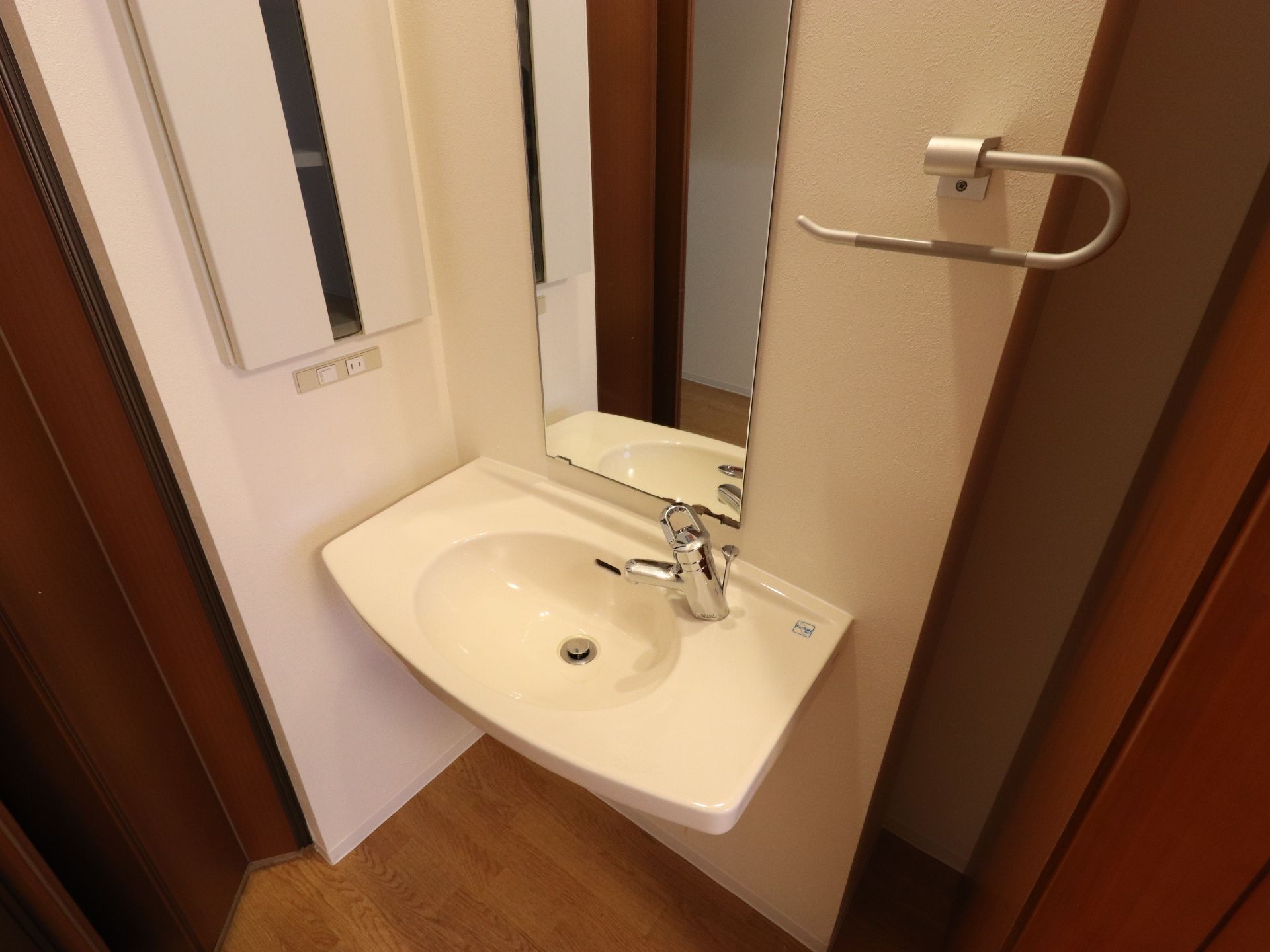 レバー式水栓になっている洗面台である。レバー一つで楽に水の量や温度を変えられる。鏡や棚をはじめ、タオル掛けが設けられている。