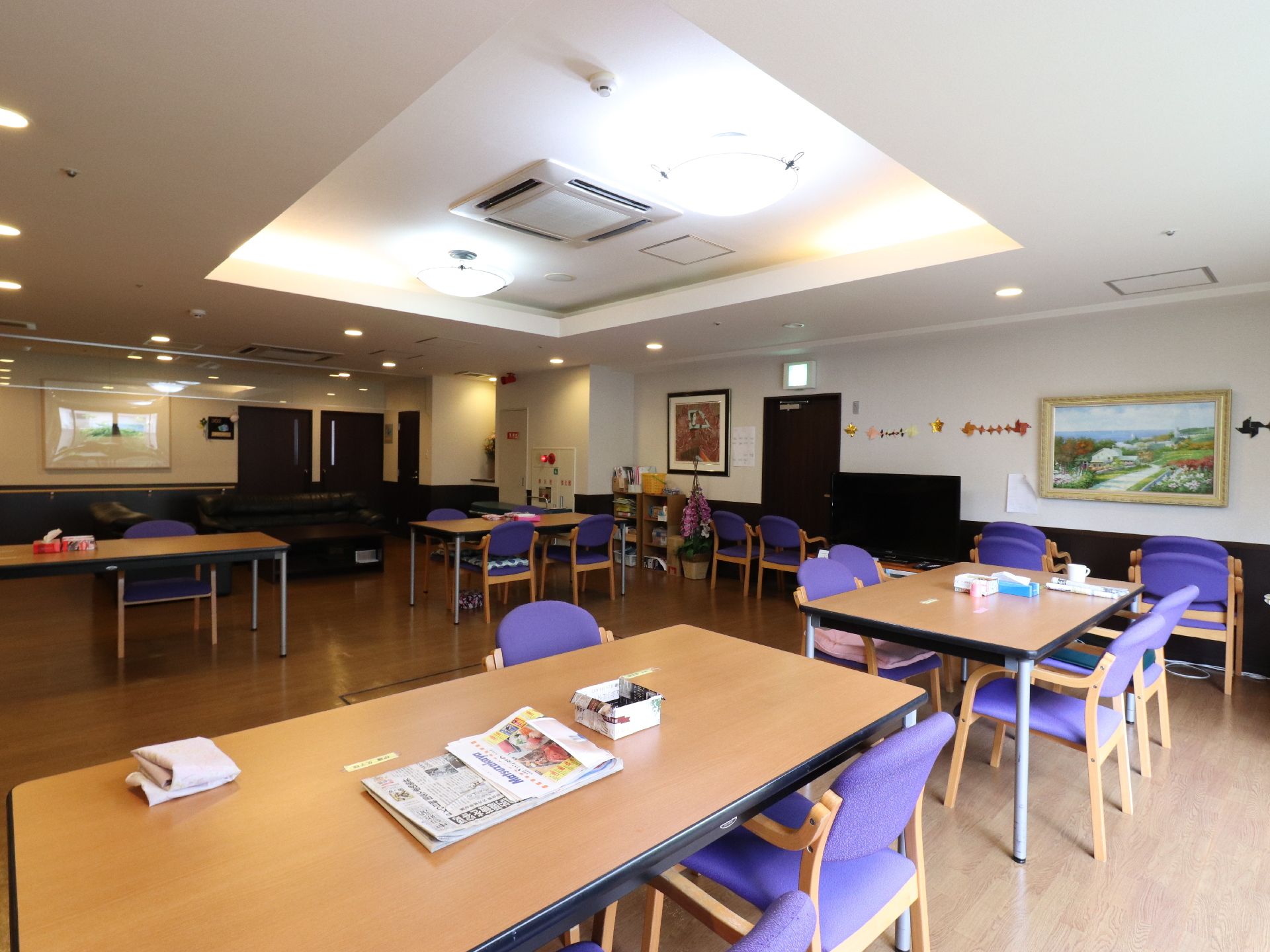 入居者たちが集まることができる大きな部屋には、紫色のシートのイスと木製のテーブルが置かれている。壁には、絵画が飾ってある。