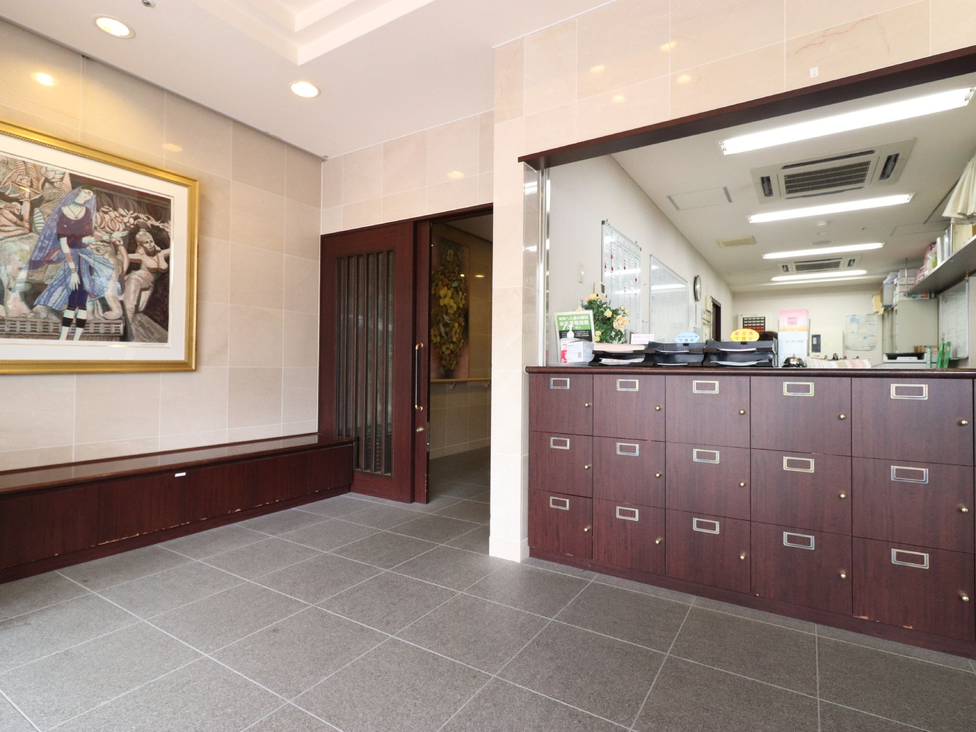 大きな絵画がエントランスに掛けられている。全体的に和風テイストの雰囲気である。来客用の下駄箱の奥は受付である。