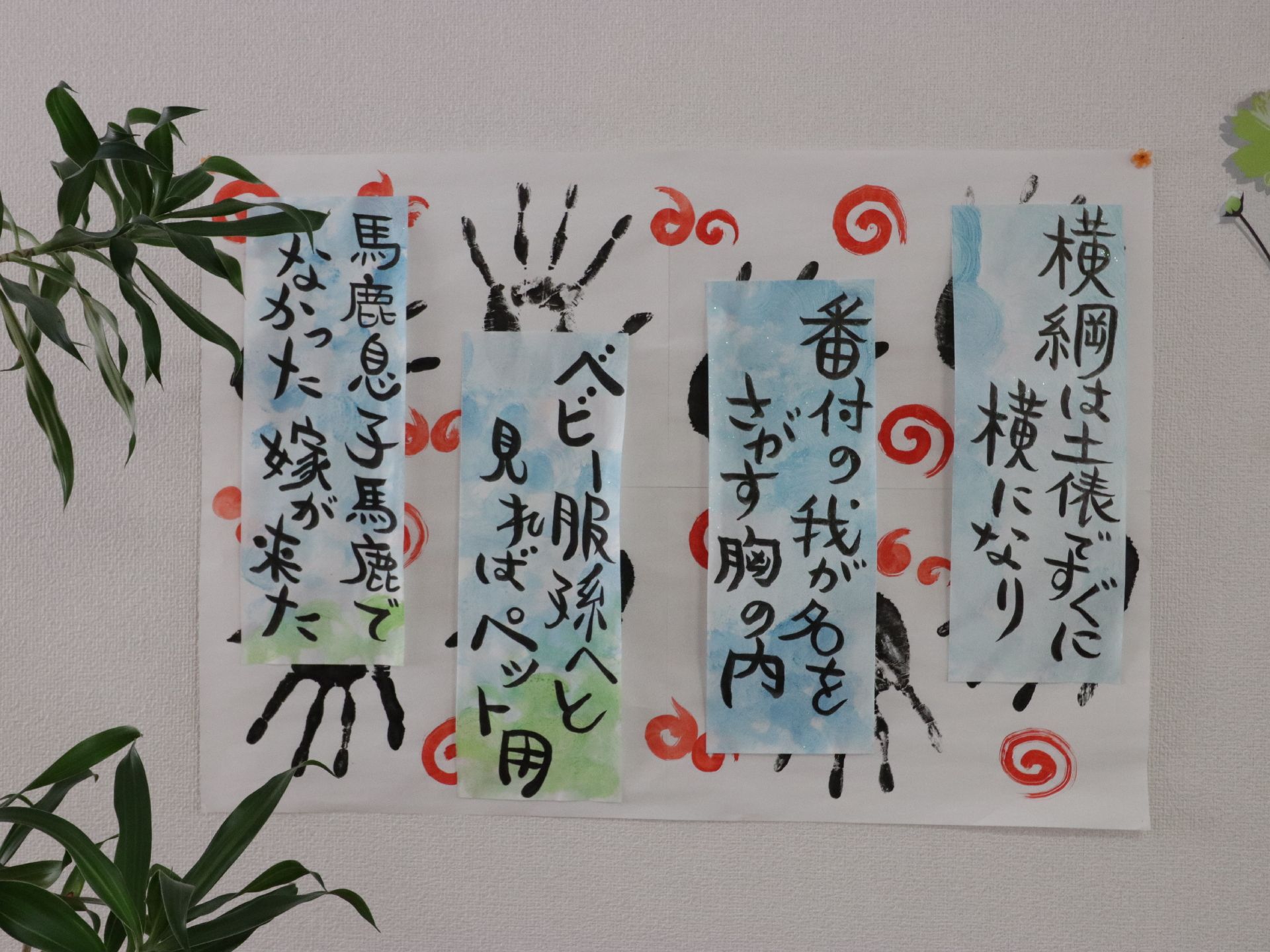 壁に４つの俳句が展示されている。その下に貼られた紙には手形がおされている。そばに観葉植物が置いてある。