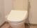 フラットなフロアにトイレが設置されている。便器とタンクはアイボリーで、白い温水洗浄便座が取り付けられている。