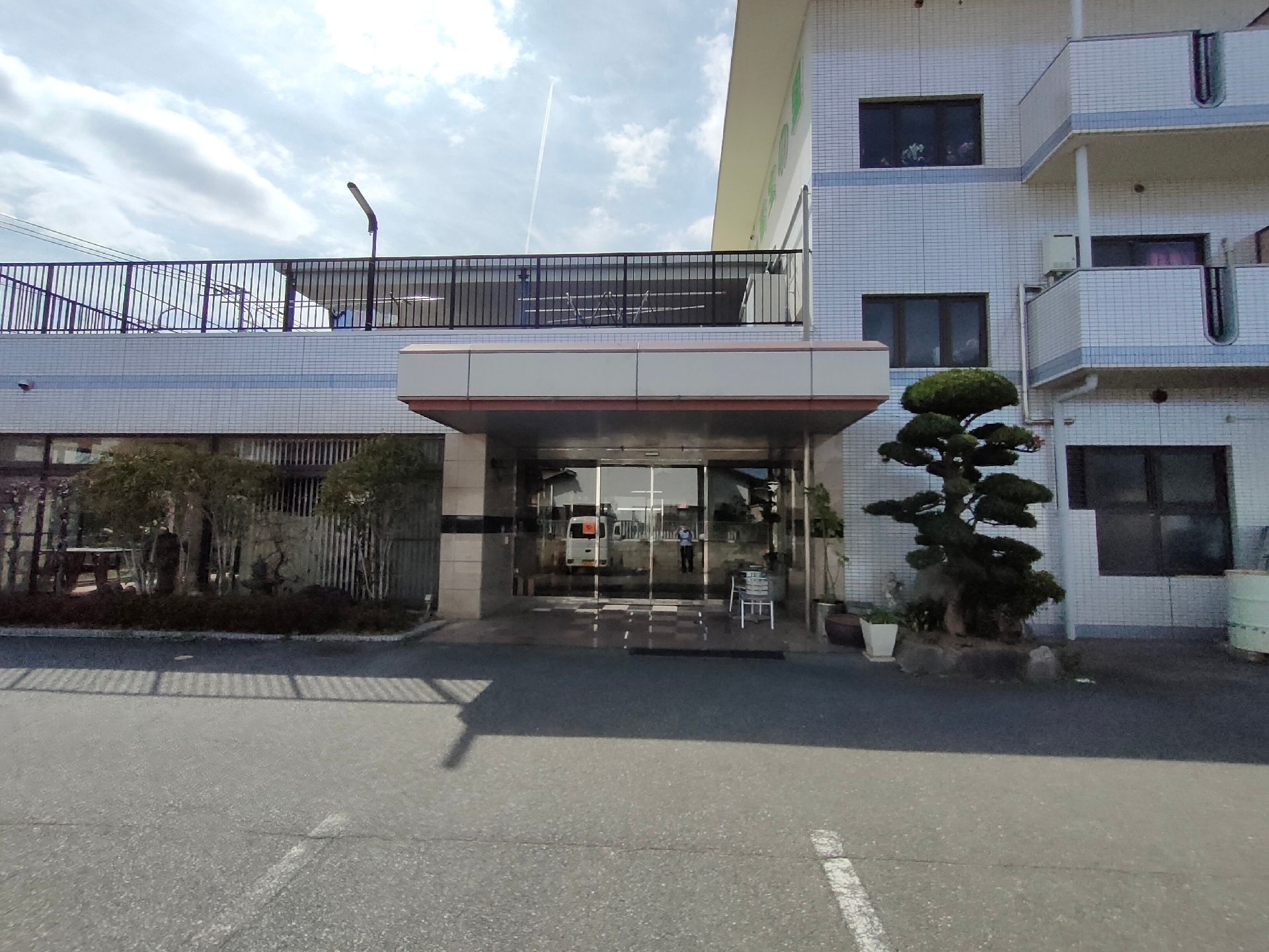 施設の入り口前には植物が植えられた鉢植えが複数置かれている。玄関はドアとその横がガラス張りで中の様子が見える。