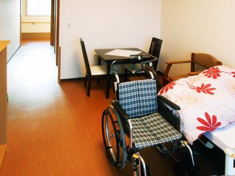 ふたり掛けのテーブルセット、車椅子、ベッドが置かれたひとり用の居室