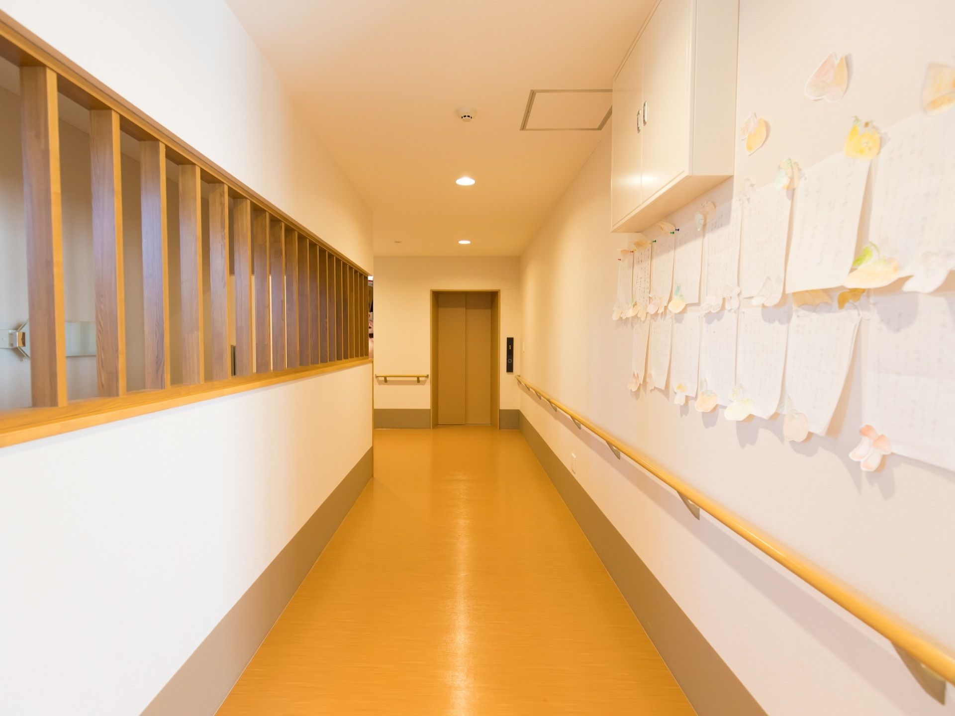 廊下の壁には掲示物が貼られ、つきあたりには、エレベーターが見える。白い壁は傷などがなく、明るく、清潔感がある。