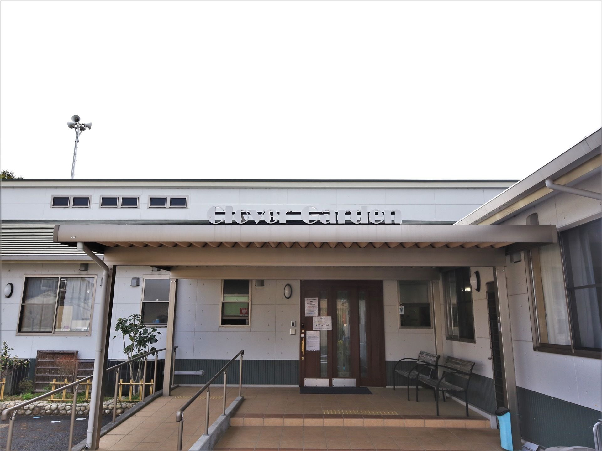 玄関の前面には屋根がかけられており、施設名称を英語表記した表示板が設置されている。玄関扉の前にベンチが並べられている。