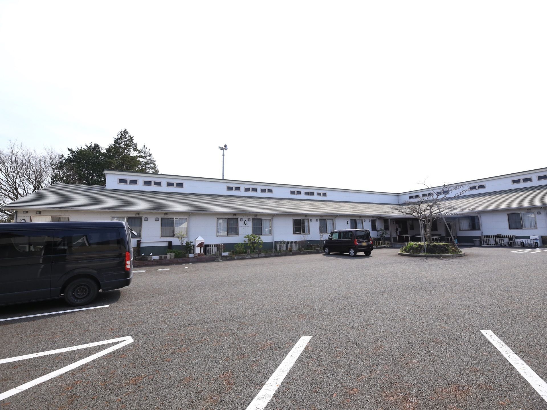 L字型の建物の前にアスファルトで舗装されたスペースが広がっている。自動車を置くための区画が明示されていて駐車しやすい。
