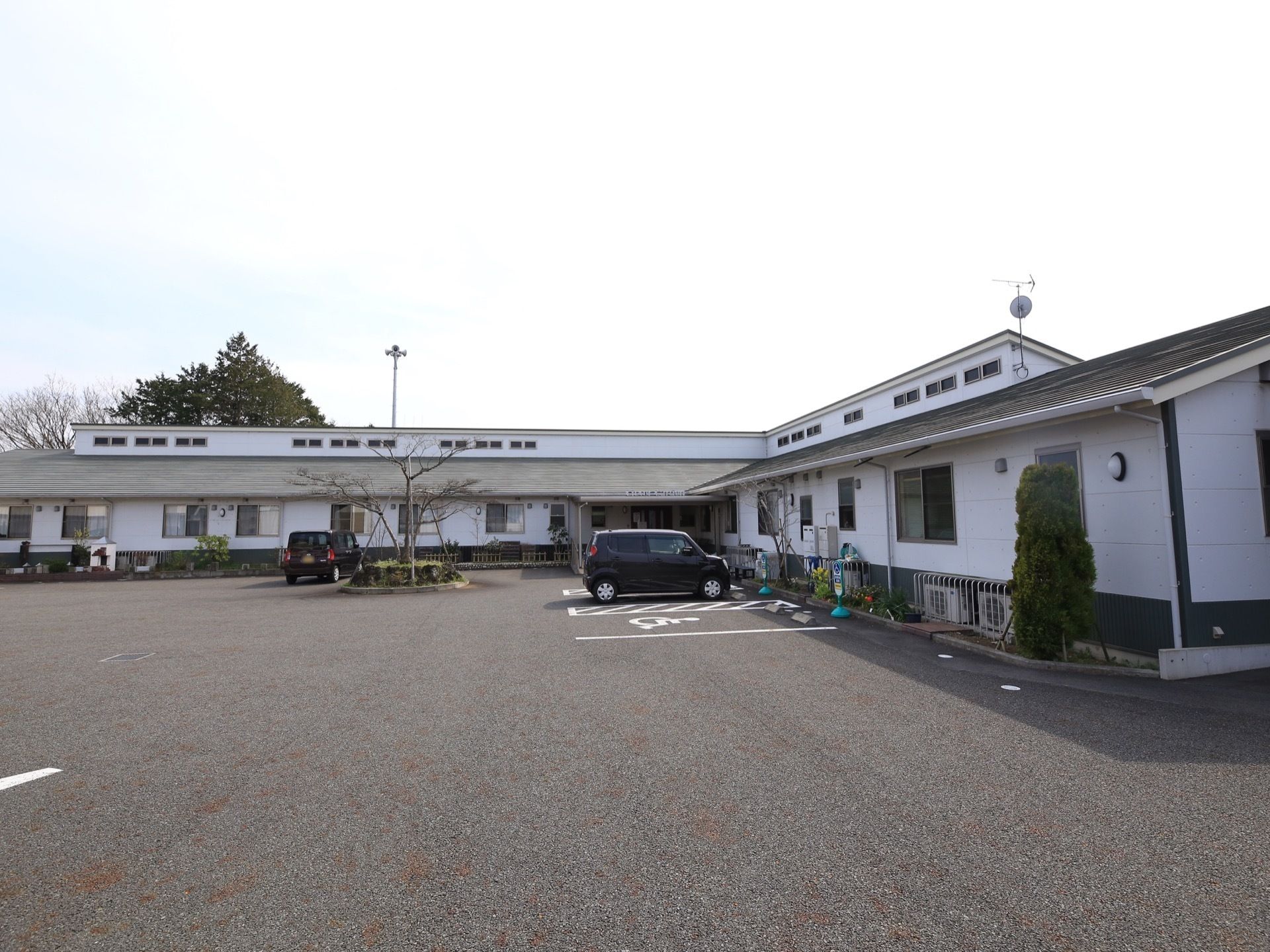 アスファルトで舗装された広々とした敷地に、L字型の施設がある。建物周辺やロータリーに植栽が施されている。