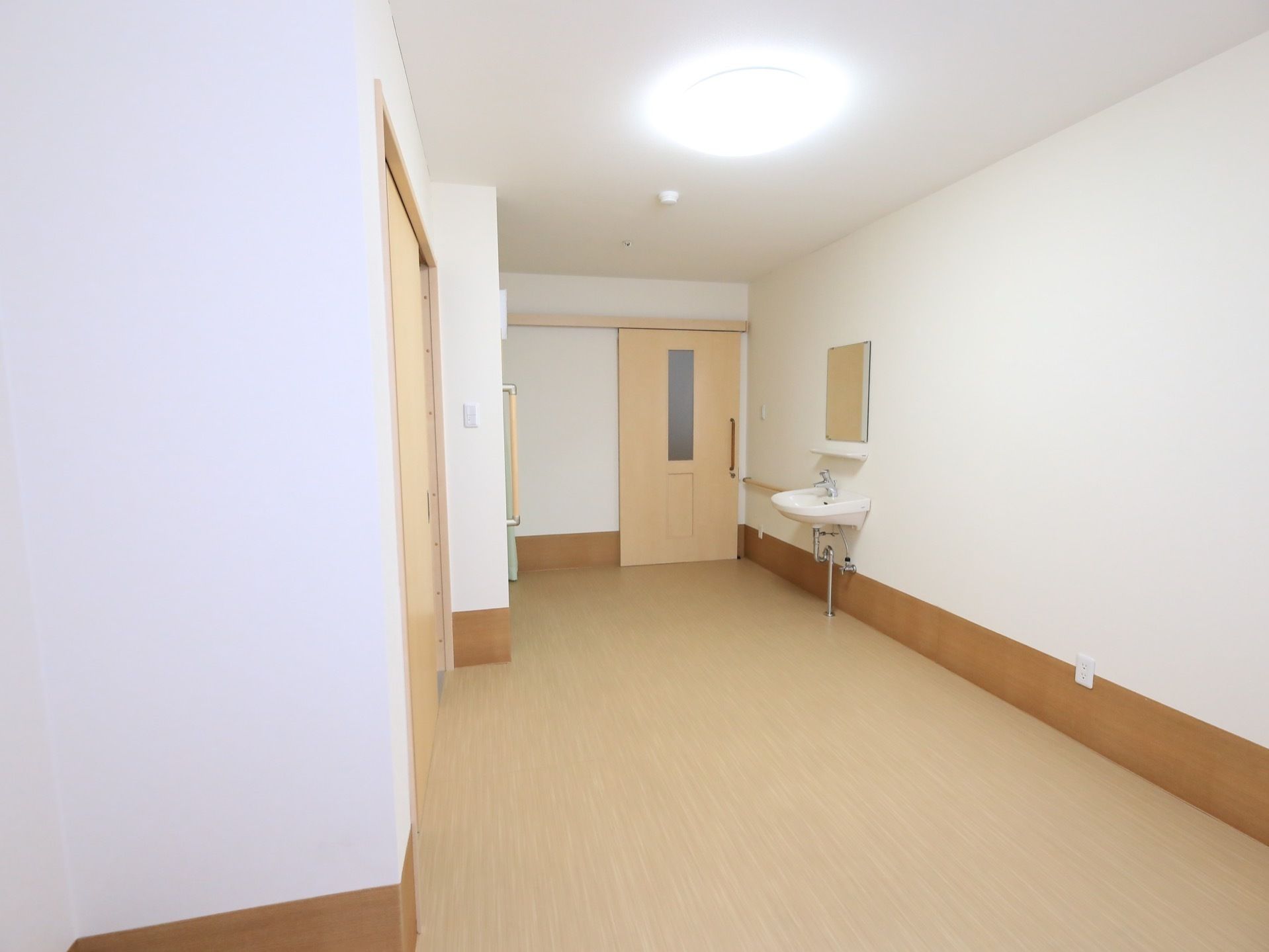 入り口付近に比べると部屋の中央部の横幅が広くなっており、部屋の奥は更に広がっている。右側に洗面台と鏡が見える。