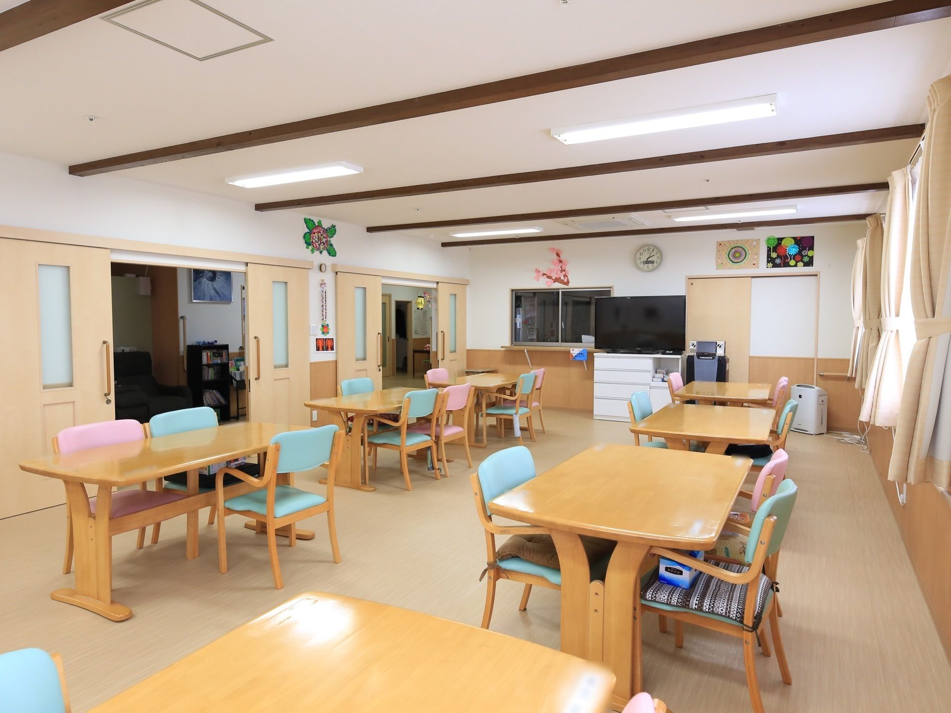 広間にダイニングセットが並べられている。椅子の背もたれには3色のパステルカラーが用いられており、カラフルで明るい印象を与える。