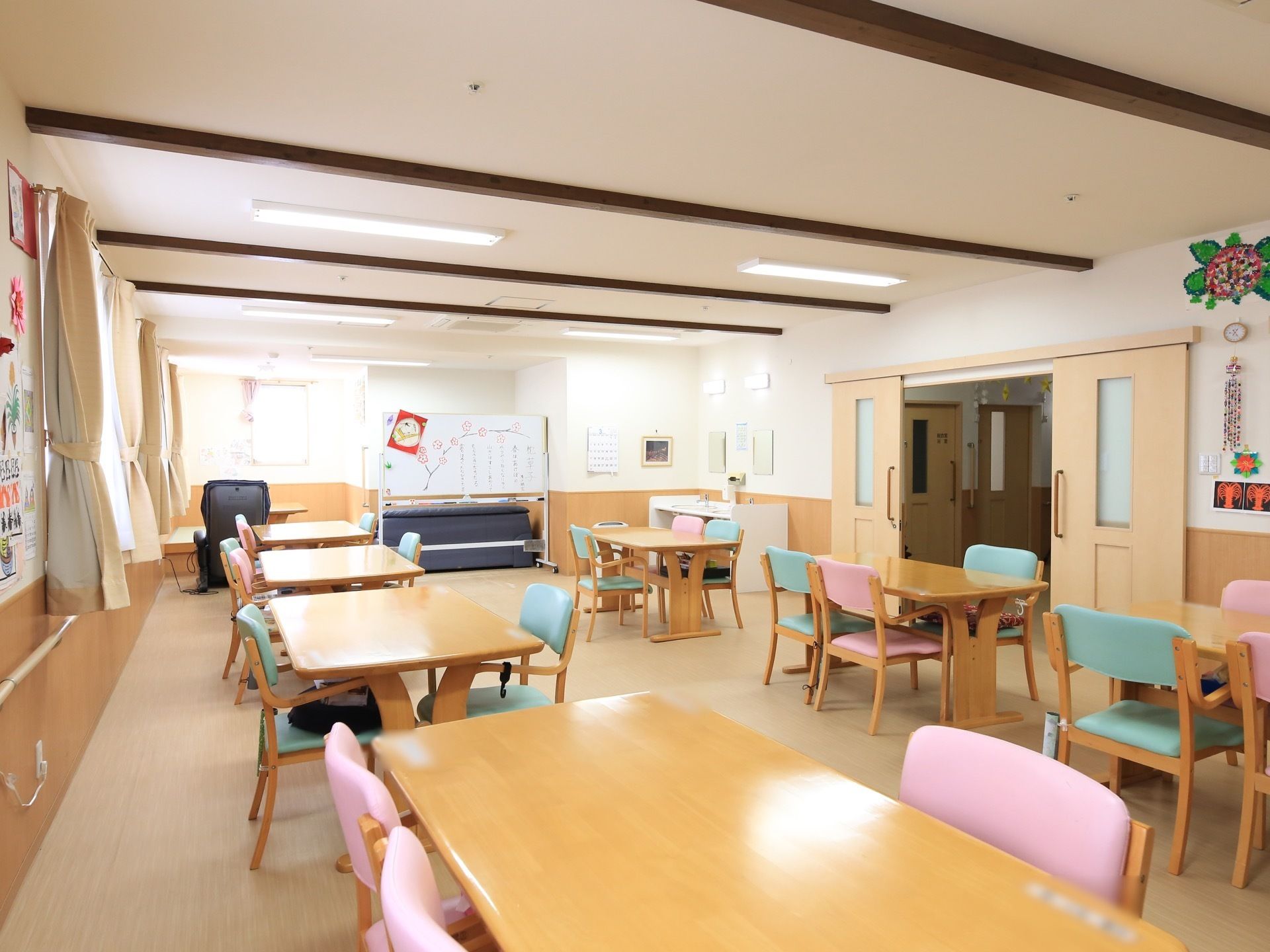 ダイニングセットが整然と並べられた広間。椅子の背もたれに複数の色が用いられており、快活で明るい印象を与える。