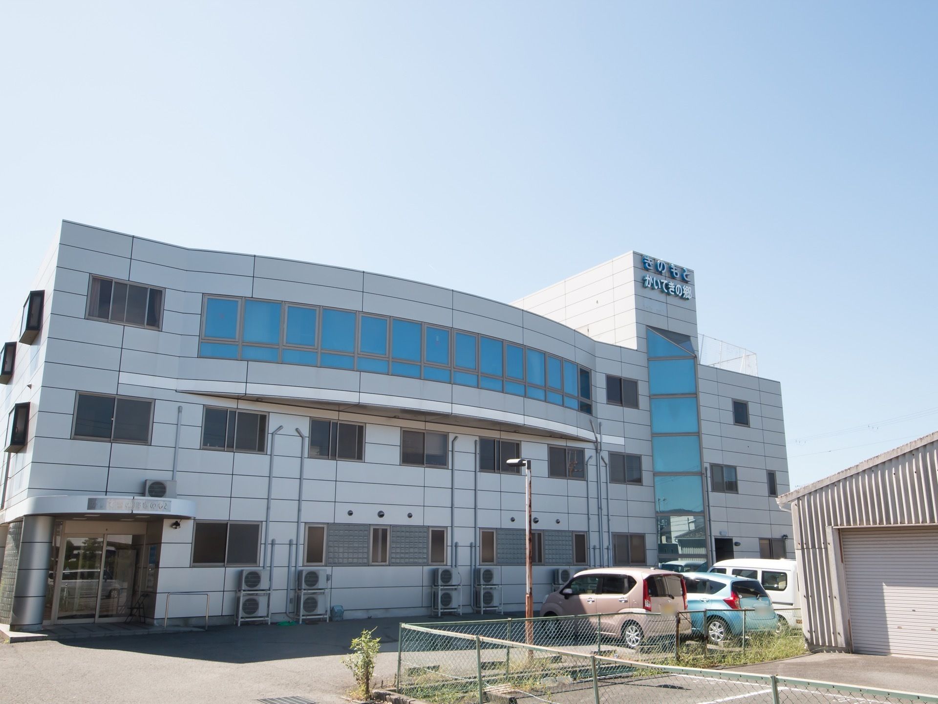 グレーで統一された、スタイリッシュな施設である。地上３階建てである。複数の窓が設置されている。駐車場も完備。