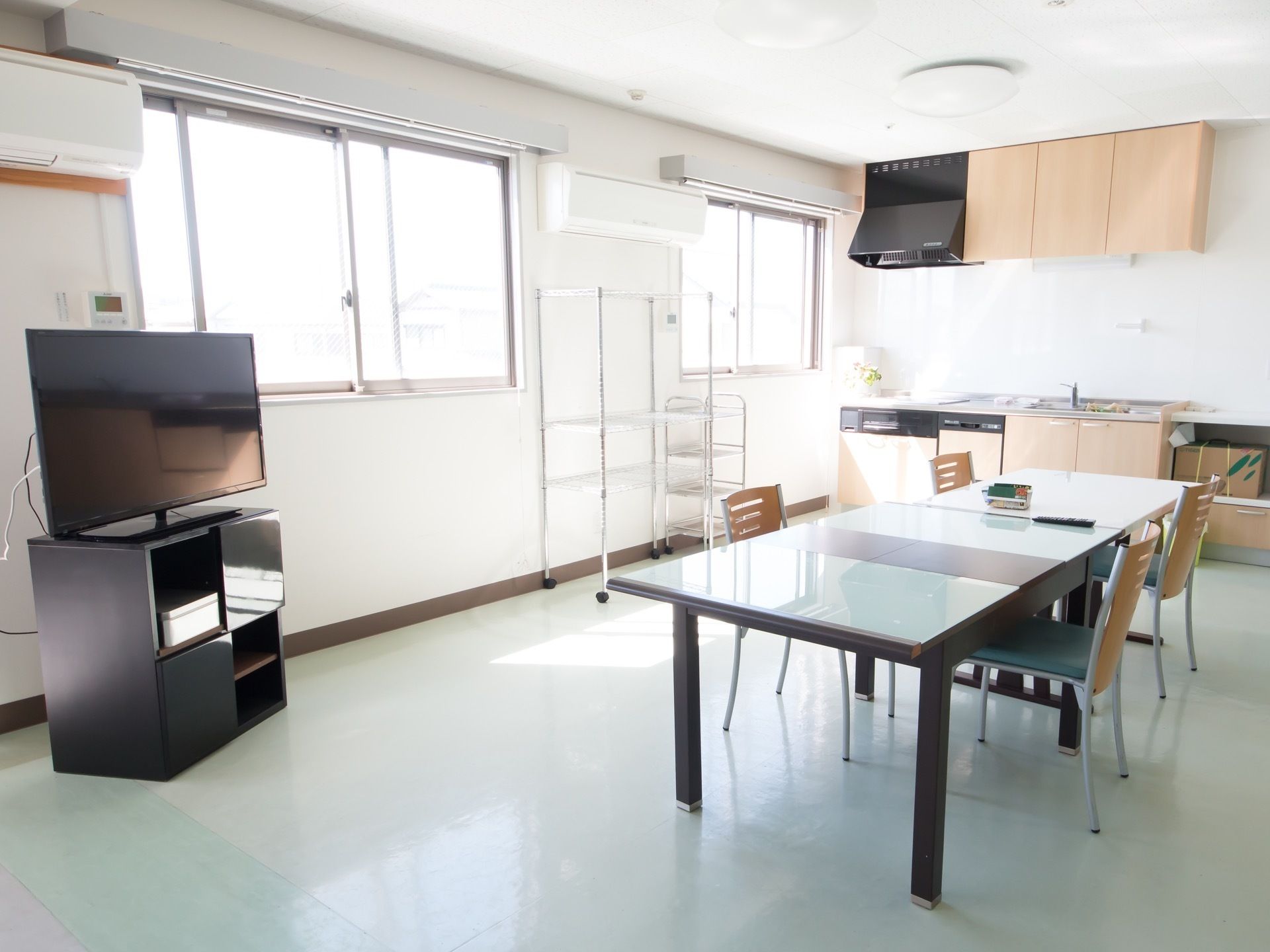 落ち着いた床色の多目的室である。窓が２枚設置されており、日差しがはいっている。システムキッチンやテーブルセットを完備。