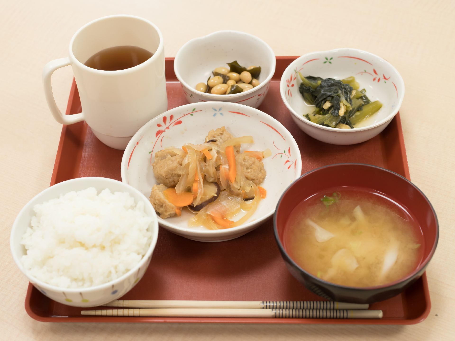 煮物などおかずが３品と、お味噌汁、ごはん、お茶がのせられたトレー