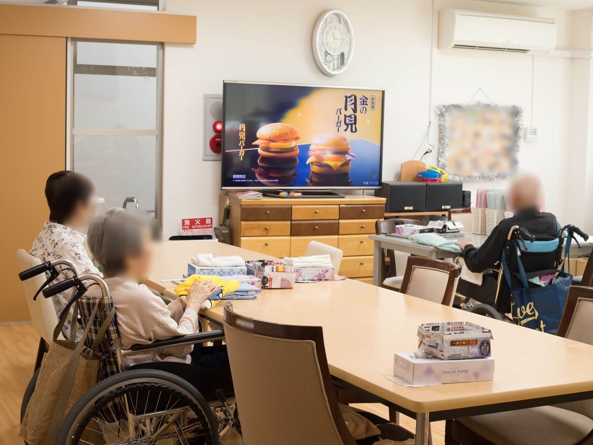 それぞれの車椅子や椅子などでテレビを見ながらリビングルームで寛ぐ入居者たち