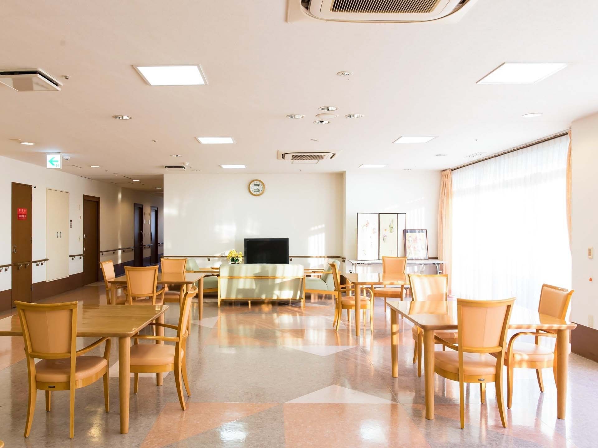 窓から日差しが差し込む空間に、テーブルセットやテレビを配置している。テーブルの間をあけ、通路を確保している。