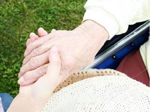 屋外で車椅子に乗った女性の手をそっと握り返す介助スタッフ