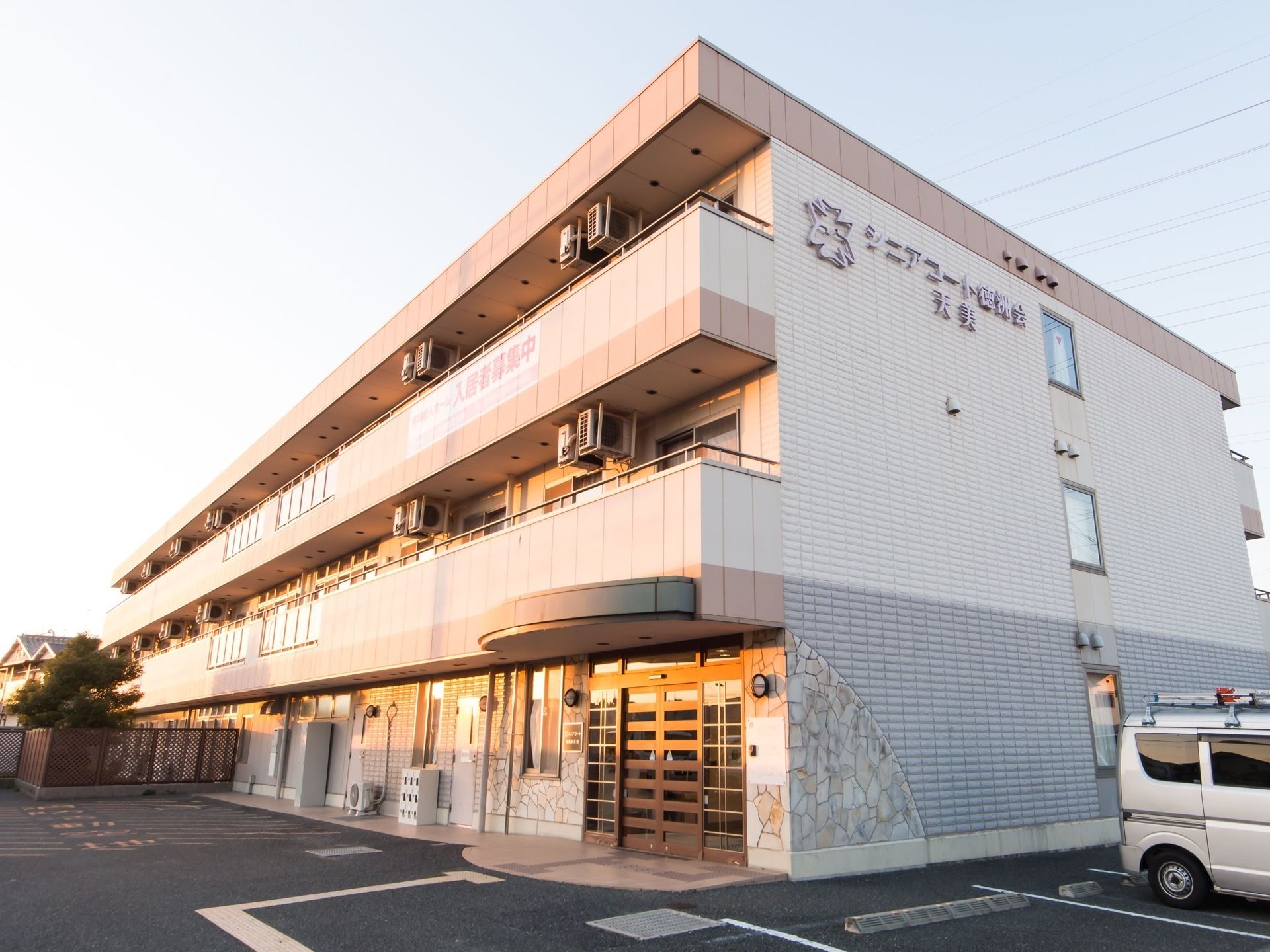 3階建てで2階と3階には、ベランダがある。3階のベランダには、入居者募集と書かれている。玄関の右側に、駐車場が付いている。