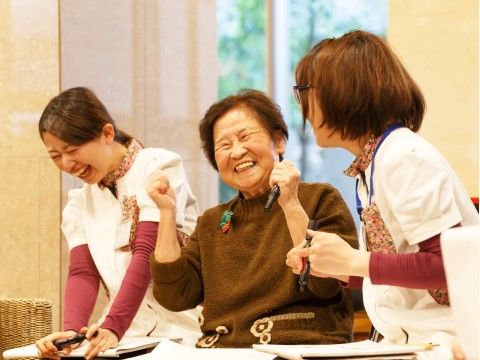 レクリエーション中に笑顔で盛り上がる女性の入居者と２名の施設スタッフ