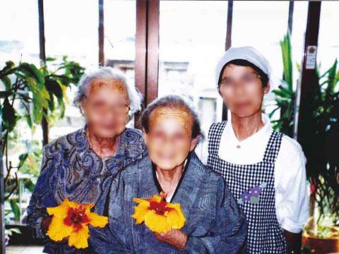 ハイビスカスの花を持って微笑む２名の入居者と１名の調理スタッフ