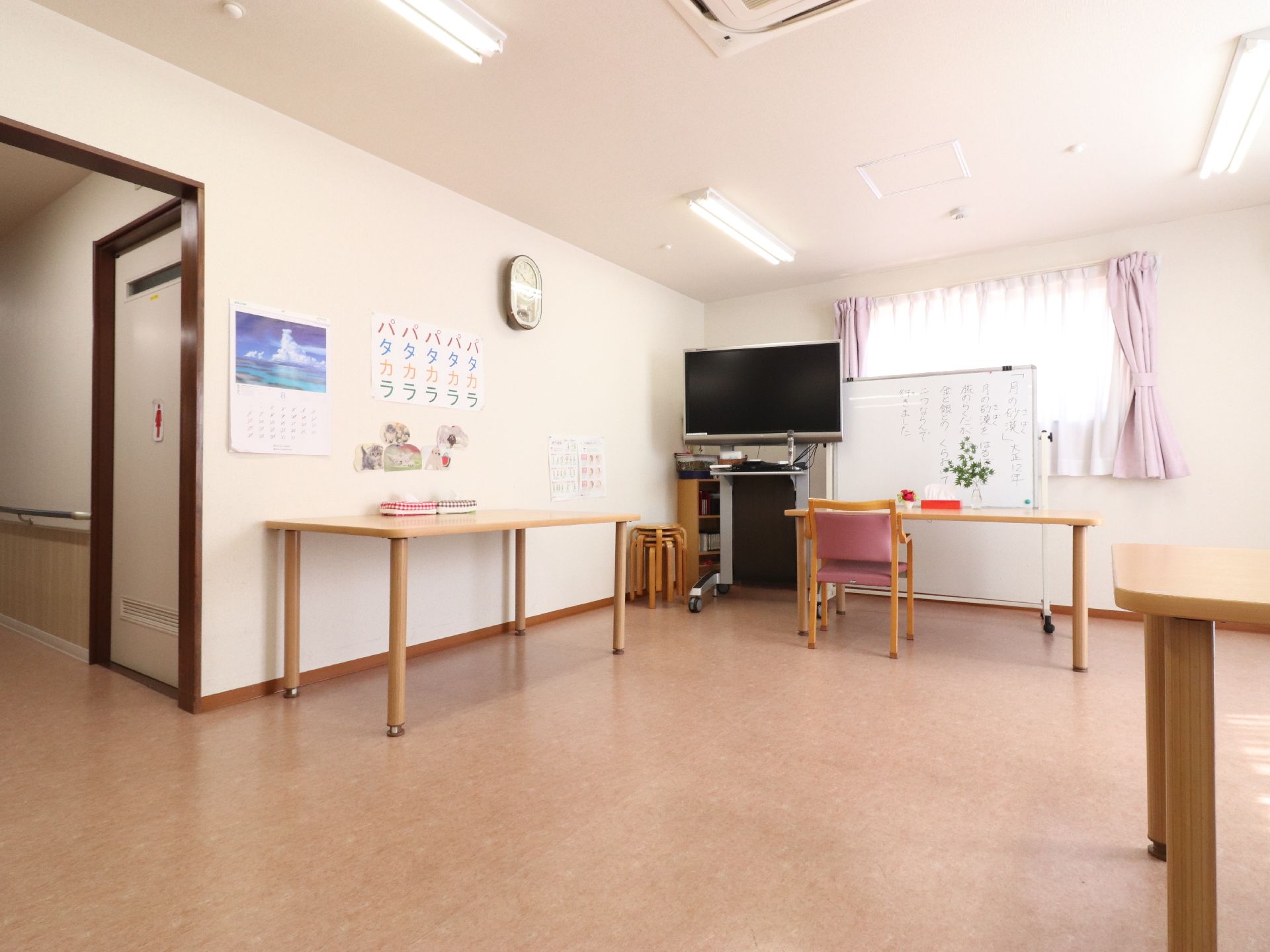 ダイニングルームには、テーブルと椅子が置かれている。背の高いテレビ台に設置されたテレビがある。ホワイトボードがある。