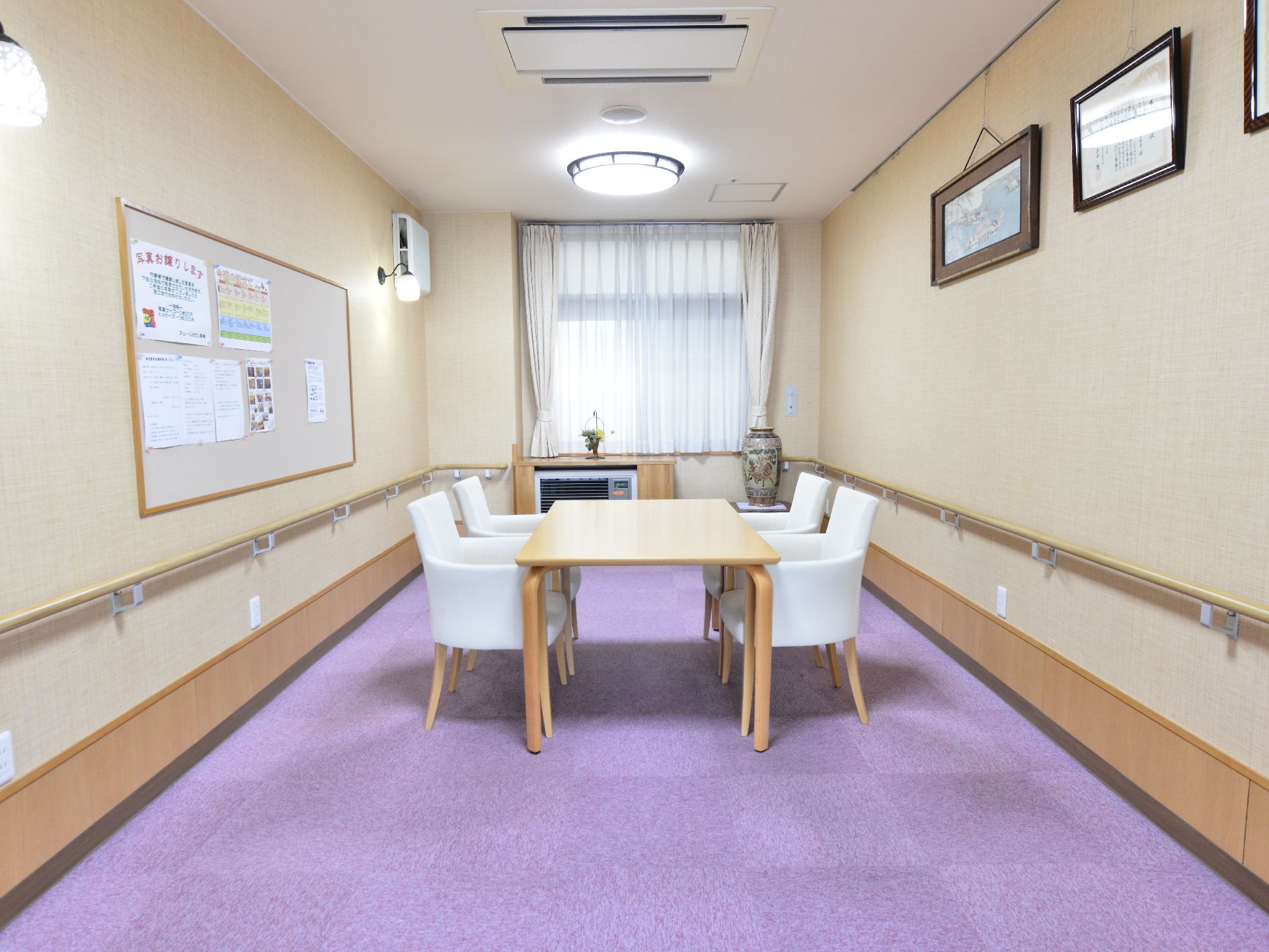 談話室の床にはパープル系のカーペットが敷き詰められている。日差しを取り込む腰高窓が1つあり、壁には額が掛かっている。