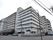 施設は道路の曲がり角部分に建てられた8階建てのマンションである。外壁はベージュ系で、屋根には施設名が表示されている。