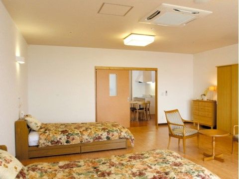 木目調の家具と花柄のベッドカバーが華やかな印象の２人用居室