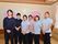 背後に時計と桜の絵が貼りだされている所に、6人のスタッフが顔を揃えている。内訳は4人の女性スタッフと2人の男性スタッフとなっている。