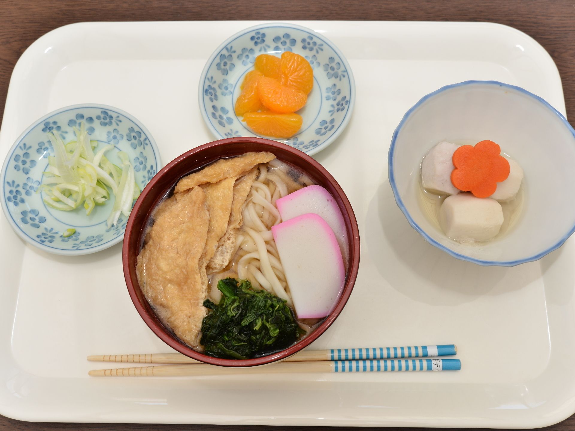 お盆にのせられた5種類の食事が写っている。ハンバーグ、なめこ汁、わかめご飯といったものがあり、手前には箸もある。