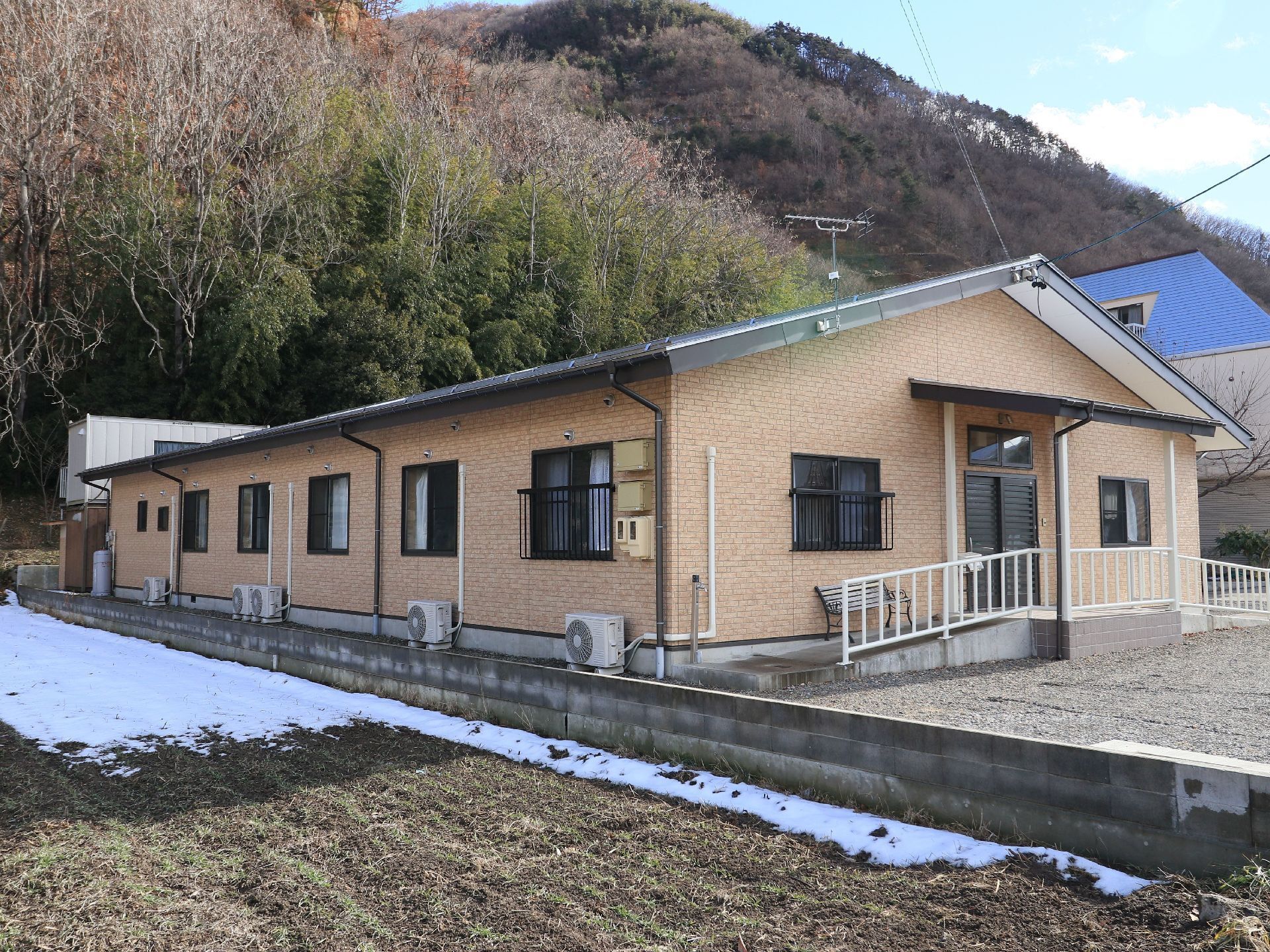 入り口までは緩い傾斜になっている。扉の横にはインターフォンが設置され、建物の下には駐車スペースもある。